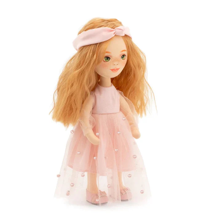 Red-haired doll with green eyes and freckles wearing a pink headband, tulle dress with pearls, and pink shoes.