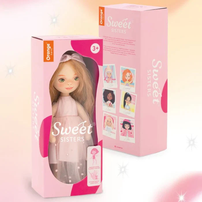 Blonde doll with green eyes in a pink tulle dress inside a pink box, next to a box showing other dolls in the series.