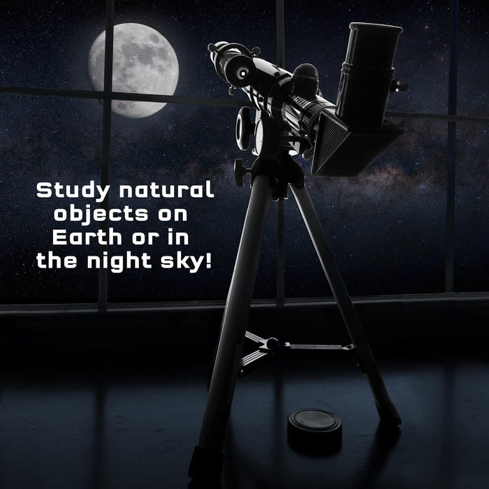 Black telescope on a tripod silhouetted against a large moon and starry night sky through a window.