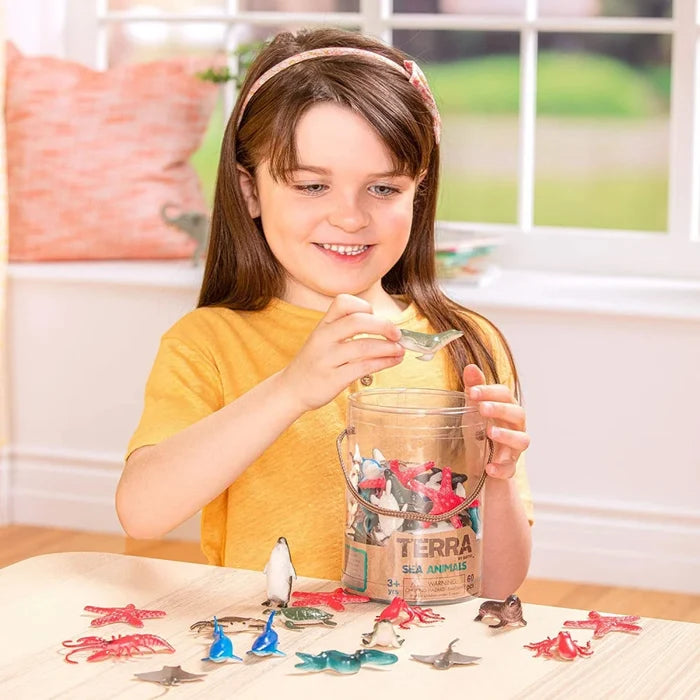 Girl playing with colorful plastic sea animal figurines like starfish and rays from a clear tube on a wooden table.