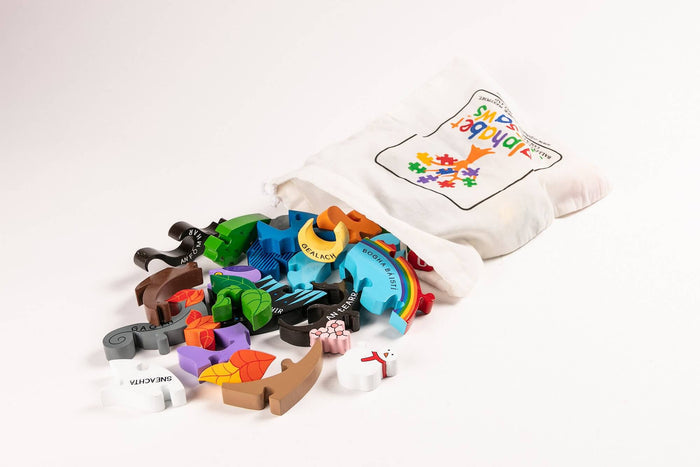 Colorful wooden jigsaw pieces with Irish text spilling out of a white drawstring bag with a puzzle tree logo.