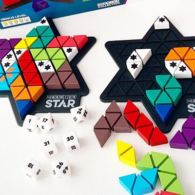 Two black star-shaped puzzle boards with colorful triangular pieces, numbered dice, and star-marked blocker pieces.