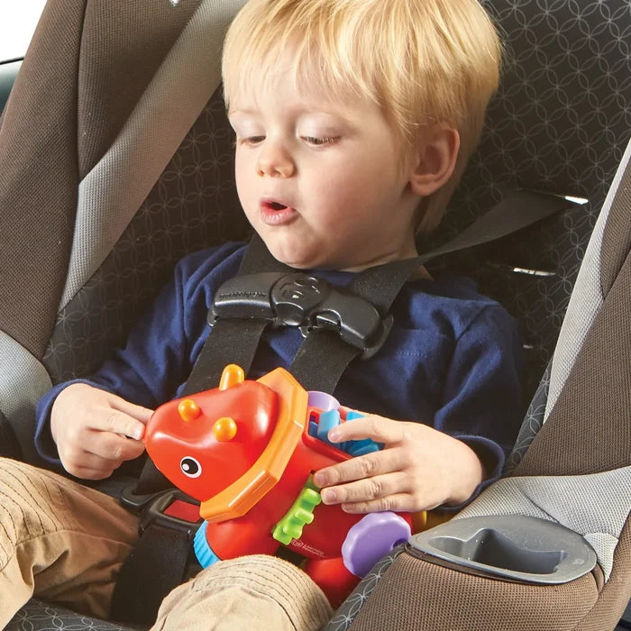 Toddler in a car seat playing with a red and orange triceratops toy featuring colorful fidget gears and buttons.