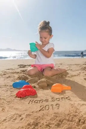 Child playing on a sunny beach with colorful red, blue, and orange plastic car and boat sand molds.