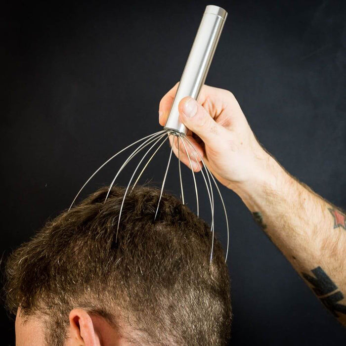 Silver scalp massager with a cylindrical handle and flexible wire prongs being used on a man's scalp.