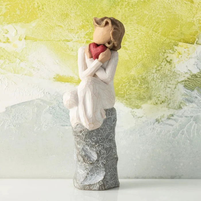 Statue of a woman holding a heart-shaped object against a textured yellow and white background