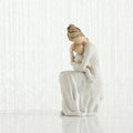 White ceramic figurine of a woman sitting with her child on a white background