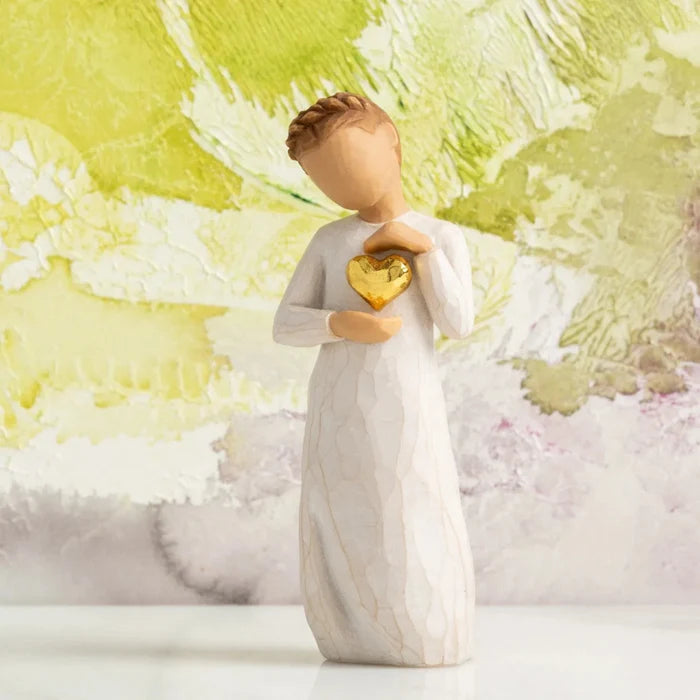 Angel figurine holding a gold heart against a colorful abstract background
