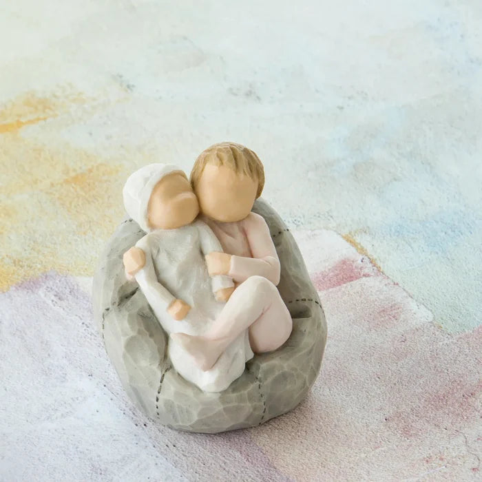 Decorative figurine of two children embracing on a stone base against a soft, multicolored background