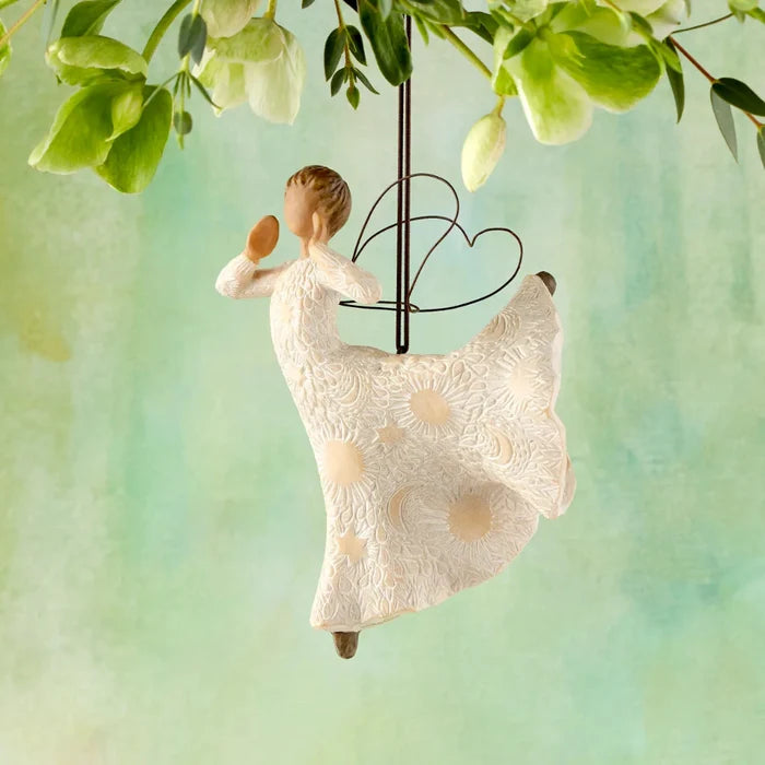 Decorative figurine of a woman in a white dress with moon and stars and suns , hanging from green leaves against a soft green background.