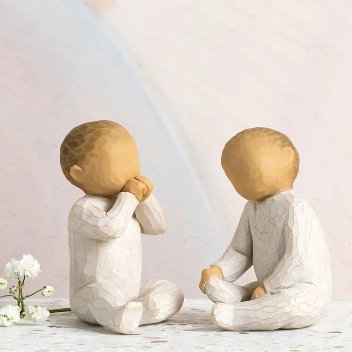 Two stone sculptures of children sitting on a surface with a light background