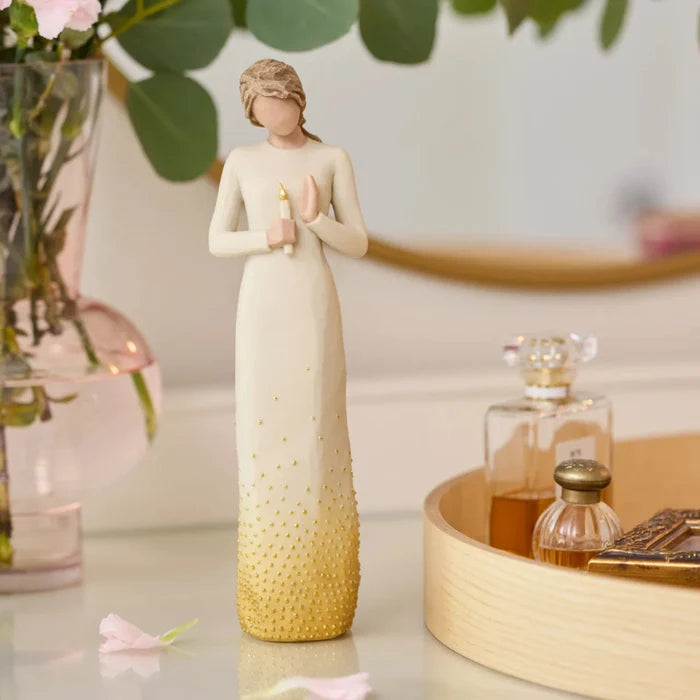 Decorative figurine of a woman holding flowers on a table with a vase and perfume bottles in the background.