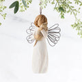 Angel figurine with wire wings hanging against a light background with greenery