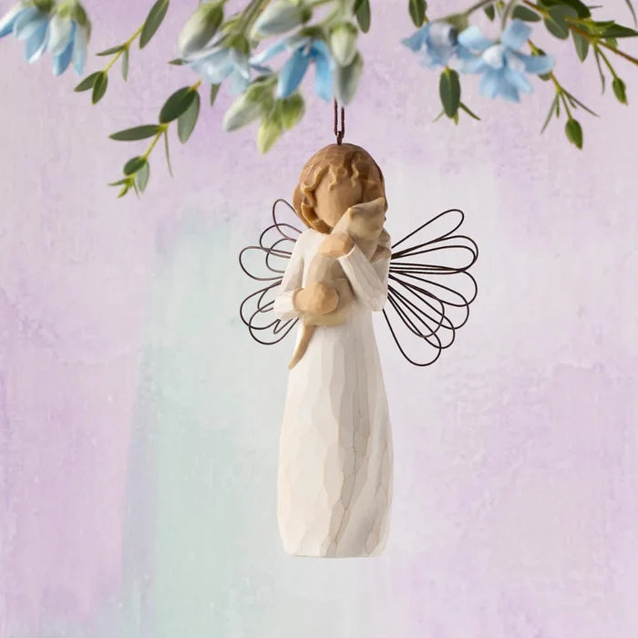 Angel figurine with outstretched wings hanging from a branch with flowers on a pastel background