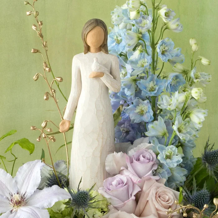 Statue of a woman in a white dress holding a white dove surrounded by flowers on a green background