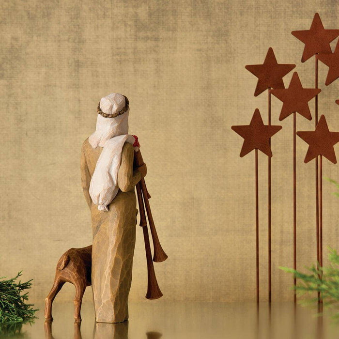 nativity scene figure with a sheep standing against a textured beige wall with star decorations.
